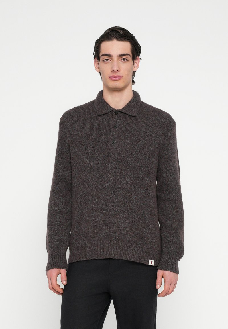 Barna kötött pulóver gallérral, három fekete gombbal és bordázott mandzsettával. Az anyag puha, texturált megjelenésű.