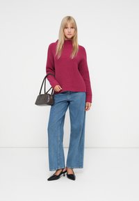 Sweater às riscas em tons de castanho, calças de ganga azuis de perna larga e sapatos pretos de salto. Bolsa escura com alça curta, apresentada sobre um fundo branco.