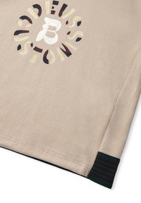 Beige tričko s vícebarevným kruhovým logem, ve středu s písmenem 'B' a vzorovými akcenty. Rukávy mají zelené a černé pruhované detaily.