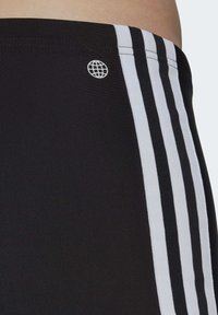 Pantalones cortos deportivos negros con tres rayas blancas a lo largo del costado, hechos de tejido suave. Presenta un pequeño logotipo de un globo blanco cerca de la cintura.