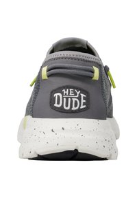 Sneaker grigio con parte superiore in tessuto morbido, suola maculata bianca e nera e logo "HEY DUDE" nero sul retro. Accenti verdi visibili.
