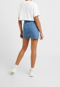 Vaaleansininen farkku-mini hame, joka on muotoiltu istuvaksi. Yhdistettynä lyhytmalliseen valkoiseen t-paitaan ja valkoisiin tennareihin, joissa on näkyvät nauhat.