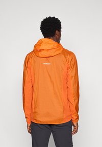 Letvægts vandtæt jakke i orange med en struktureret overflade, justerbar hætte og diskret branding på ryggen.