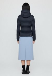 Navy puffer jacket with horizontal stitching, attached hood, and logo patch at the hem, paired with a light blue, knee-length skirt.