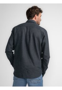 Donkergrijze overhemdd met een gestructureerde stof, lange mouwen, afgeronde zoom en een subtiel patroon. Casual ontwerp gecombineerd met blauwe jeans.