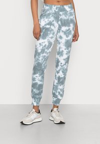 Light blue and white tie-dye joggers with ribbed cuffs and a fitted waistband. Paired with neutral-toned athletic shoes. Smooth fabric texture.