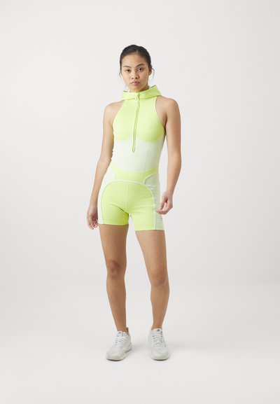 Neon zöld bodysuit, elöl cipzárral és kapucnival, színekre osztott részletekkel világosabb árnyalatokban az oldalain és rövidnadrág szabásban.