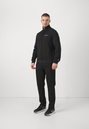 Chándal deportivo negro de tejido suave, con chaqueta con cremallera y bolsillos laterales, y pantalones a juego, ambos con detalle de logo.