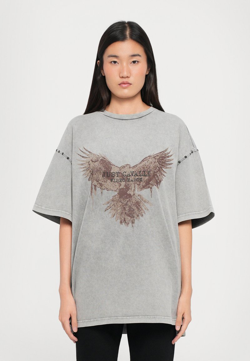 Grijze oversized t-shirt van zachte stof met een grote adelaar grafiek en de tekst "JUST CAVALLI KID EARTH" in bruin. Korte mouwen en ronde hals.