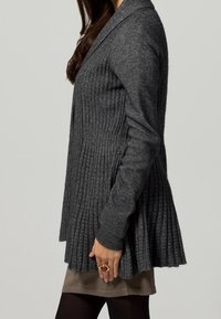 Cardigan grigio a maglia con texture a costine, scollo a V e orlo pieghettato, con maniche lunghe. Indossato sopra un top chiaro.