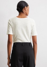 Lichtbeige shirt met korte mouwen, gemaakt van gestructureerde stof, met een ronde hals, gedragen met zwarte hoge taillebroek.