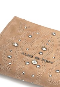 Cartera de ante beige con costuras decorativas, tachuelas metálicas y rhinestones. El nombre de la marca "ALMA EN PENA" está grabado en plata.