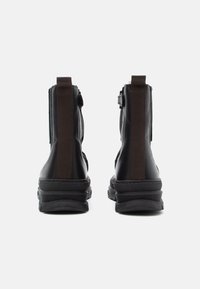 Bottines en cuir noir avec des panneaux élastiques latéraux marron, bout arrondi et semelles en caoutchouc texturé ; design épuré et minimaliste.