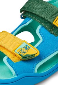 Infradito colorate con una base blu, cinturini verdi e gialli, e un logo di orso su un accento giallo. Realizzati con materiali morbidi e con un design a taglio.