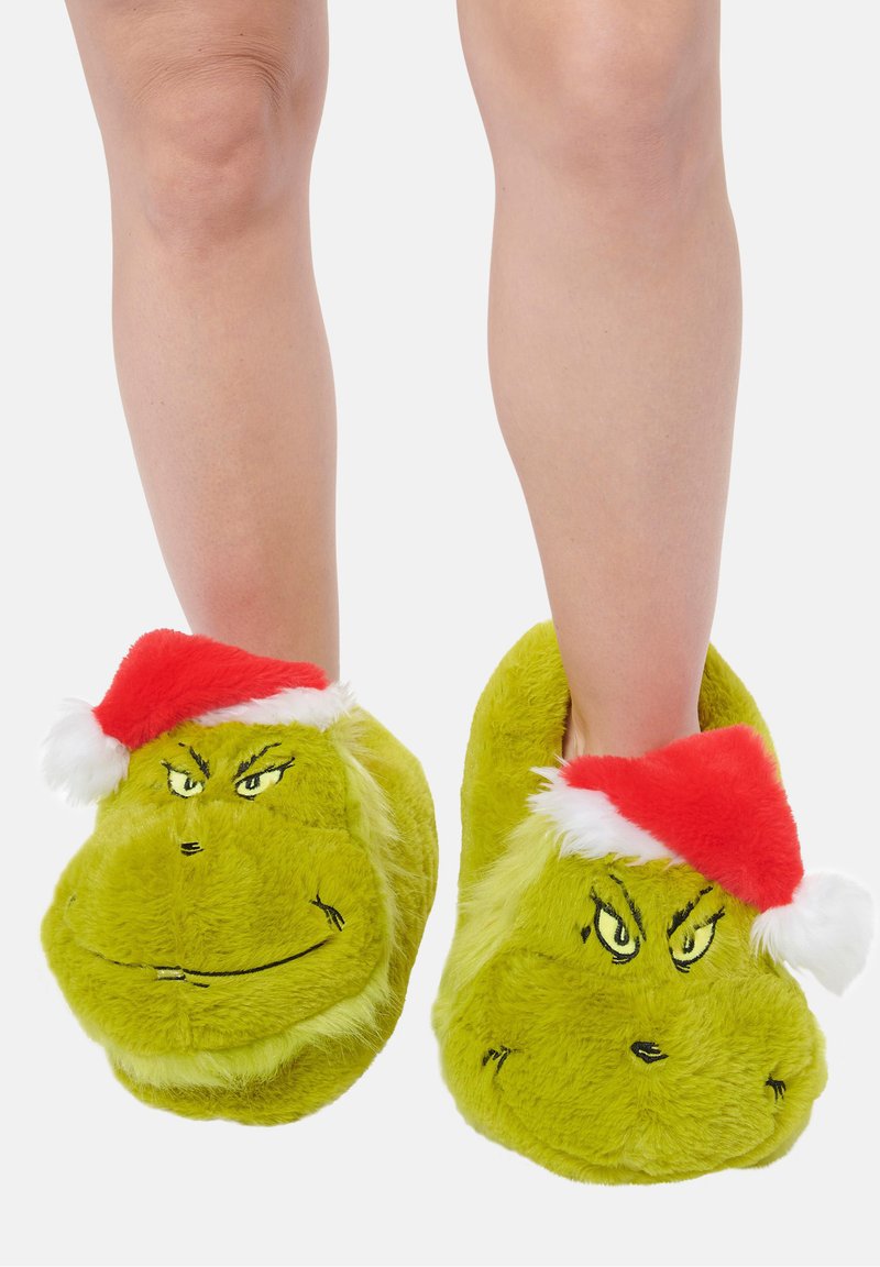 Pantofole verdi in peluche con design facciale del Grinch, dotate di un berretto di Natale rosso. Texture morbida con caratteristiche ricamate.