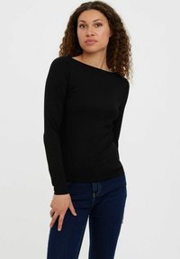 Chemise noire à manches longues en tissu doux, avec un col bateau et une coupe slim, assortie à un jean bleu foncé.