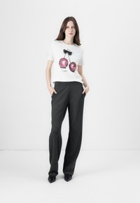 Hvid t-shirt med pink kirsebærgrafik og sort sløjfe, parret med mørkegrå, vidde bukser. Glat stof, afslappet design.