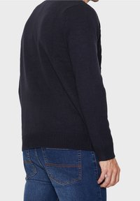 Navy knitted sweater with a ribbed texture, round neckline, and long sleeves, paired with blue jeans featuring back pockets.