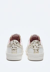 Sneakers bianche con una tomaia in pelle testurizzata, rivestimento rosa e un accento in stampa leopardata dorata sul tallone. Suola in gomma con battistrada a motivo.