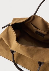 Καφέ τσάντα από καμβά με φερμουάρ, δερμάτινες λαβές και λείο εσωτερικό. Διαθέτει μία εσωτερική τσέπη και ελάχιστες ραφές.