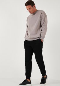 Felpa grigia chiara con spalle cadenti, polsini a coste e scollatura rotonda, abbinata a pantaloni neri a sigaretta e sneakers nere.