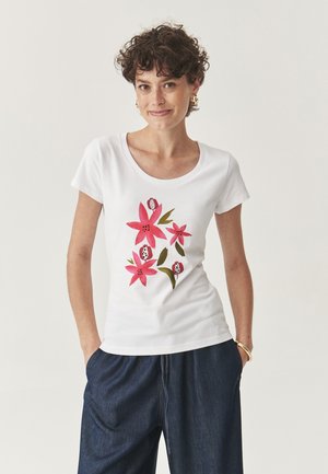 T-shirt blanc à manches courtes avec un imprimé floral en rose et vert. Le design comprend des fleurs et des feuilles stylisées.