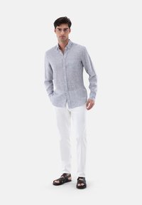 Camicia a righe blu e bianca, con colletto e taschino sul petto, abbinata a pantaloni bianchi e sandali neri.