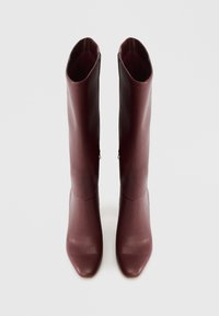 Μποτάκια έως το γόνατο σε μπορντό δέρμα με μαλακή υφή, μυτερή μύτη και ελάχιστες λεπτομέρειες ραφής, προσφέροντας μια κομψή, εφαρμοστή γραμμή.