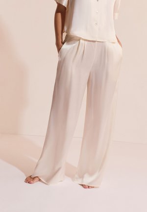 Pantalon large en satin crème porté pieds nus, associé à un haut boutonné à manches courtes en satin crème assorti.