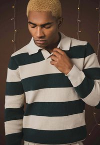 Pull-over tricoté avec des rayures alternées vert foncé et crème, doté d'un col classique et de poignets côtelés, texture lisse.