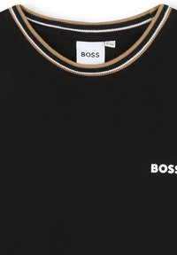 T-shirt nera con scollo rotondo, caratterizzata da un bordo a coste in contrasto dorato e bianco e un logo "BOSS" bianco sul davanti.