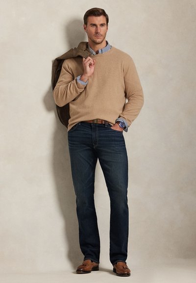 Tan pulover iz pletiva čez modro-belo črtasto srajco, temne kavbojke in rjavi loafer čevlji. Rjav blazer premetan čez ramo. Preprost, čist dizajn.