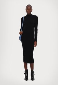 Robe midi noire en tricot avec un col haut et des manches longues, accompagnée de bottines noires à talons et d'un sac bandoulière bleu.