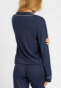 Granatowy zestaw piżamowy z kołnierzykiem i białym wykończeniem, składający się z dopasowanej bluzki i spodni, wykonany z miękkiej, gładkiej tkaniny o luźnym kroju.