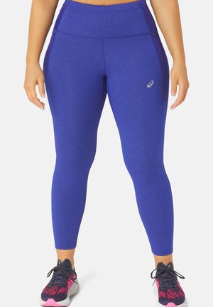 Leggings bleu royal en tissu extensible, dotés d'une taille haute et d'accents de panneaux latéraux. Associés à des chaussures de sport noires et roses.