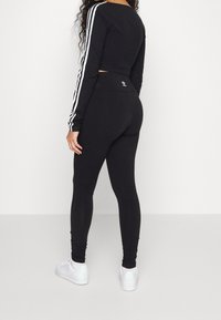 Svart kortärmad topp med lång ärm och vita ränder på ärmarna, matchad med svarta leggings. Tillbehören inkluderar vita sneakers.