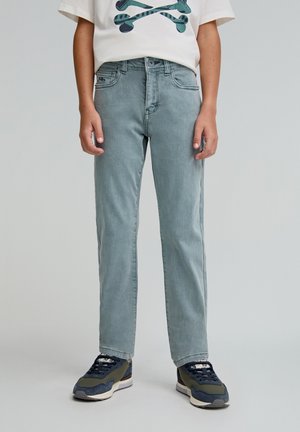 Jeans de denim azul claro con corte recto, diseño de cinco bolsillos y un sutil efecto de desgarro. Combinados con zapatillas oscuras y una camiseta gráfica blanca.