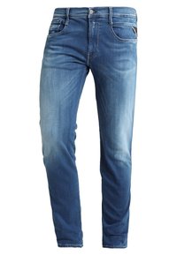 Ljusblå denimjeans med slim fit, fem fickor och silverdetaljer i midjan. Suddig textur vid låren och knäna.