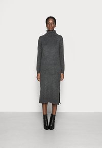 Vestito maglione grigio a collo alto, con maniche lunghe, spacchi laterali e polsini a coste. Abbinato a stivali neri alla caviglia.