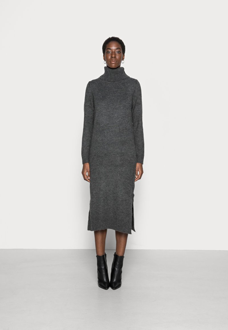 Vestito maglione grigio a collo alto, con maniche lunghe, spacchi laterali e polsini a coste. Abbinato a stivali neri alla caviglia.