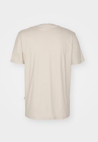 Tricou bej cu guler rotund, confecționat din bumbac moale, cu mâneci scurte și margine dreaptă, având o textură subtilă și un detaliu de branding minim.