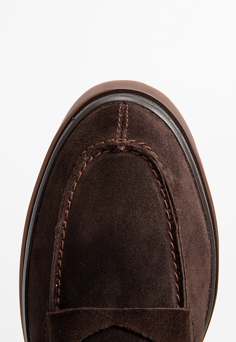 Chaussure en suede marron à enfiler avec un bout arrondi, des détails cousus et une semelle en caoutchouc contrastante. Texture lisse avec une finition mate.