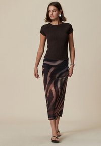 Top marrone a maniche corte con texture abbinato a una lunga gonna trasparente con motivo a strisce di tigre in tonalità terra. Sandali neri completano il look.