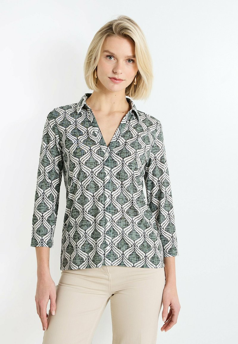 Camisa de cuello con un patrón geométrico verde y blanco, de mangas largas, con botones en la parte delantera y tejido suave.