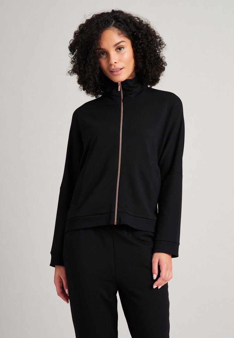 Schwarze Zip-Jacke mit hohem Kragen, ausgestattet mit einem roségoldenen Reißverschluss und zwei vorderen Taschen. Weicher, glatter Stoff in lockerem Schnitt.