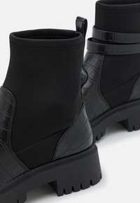 Bottines noires à tige en tissu lisse avec accents à texture crocodile, semelle épaisse et bord élastiqué pour un ajustement sécurisé.