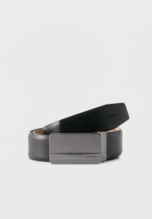 Cintura in pelle nera arrotolata con fibbia rettangolare opaca in argento, logo Calvin Klein inciso sulla fibbia e sulla punta della cintura.