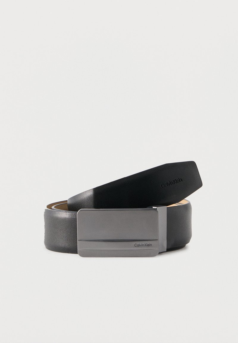 Μαύρη δερμάτινη ζώνη τυλιγμένη με ματ ασημένια ορθογώνια αγκράφα, με το λογότυπο Calvin Klein χαραγμένο στην αγκράφα και την άκρη της ζώνης.