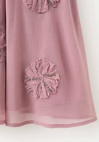 Růžové šaty z látky s texturovanými květinovými ozdobami a perlovými akcenty. Průhledný překryv a jednoduchý lem. Disponují jemnou, splývavou strukturou.