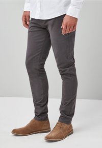 Sive slim-fit hlače od pamuka, s glatkom teksturom i suptilnim šavovima. Uparene s svijetlosmeškim antilop čizmama do gležnja.